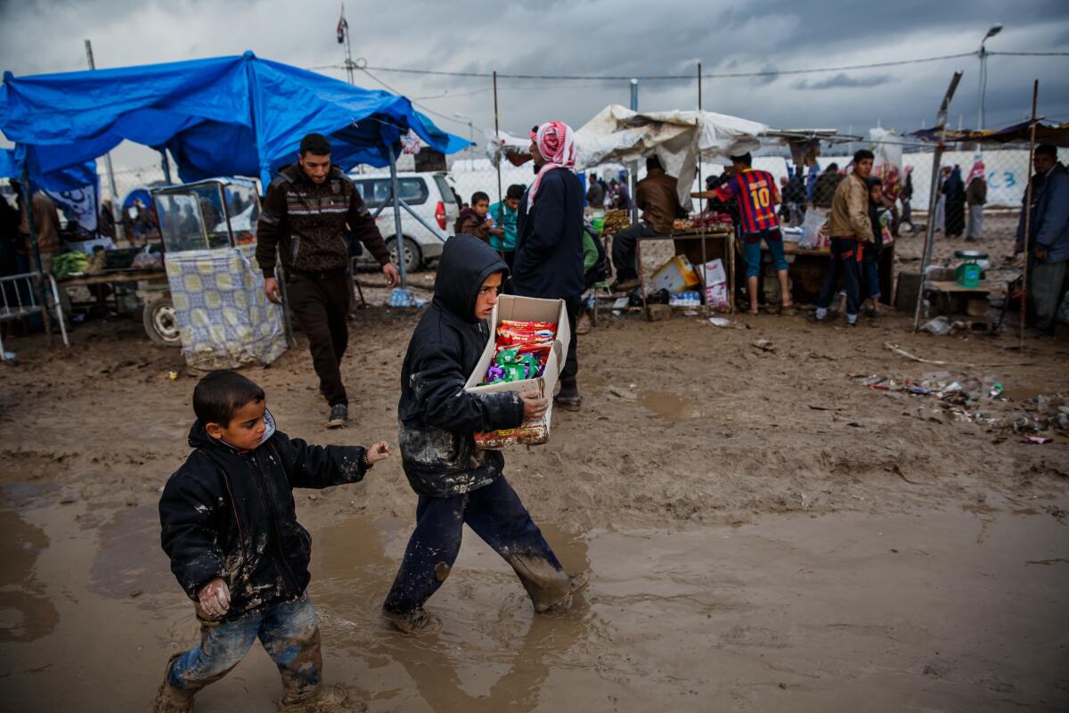 Boys carry food back to their families in the muddy and flooded areas outside the displaced persons camp in Hamam Alil.