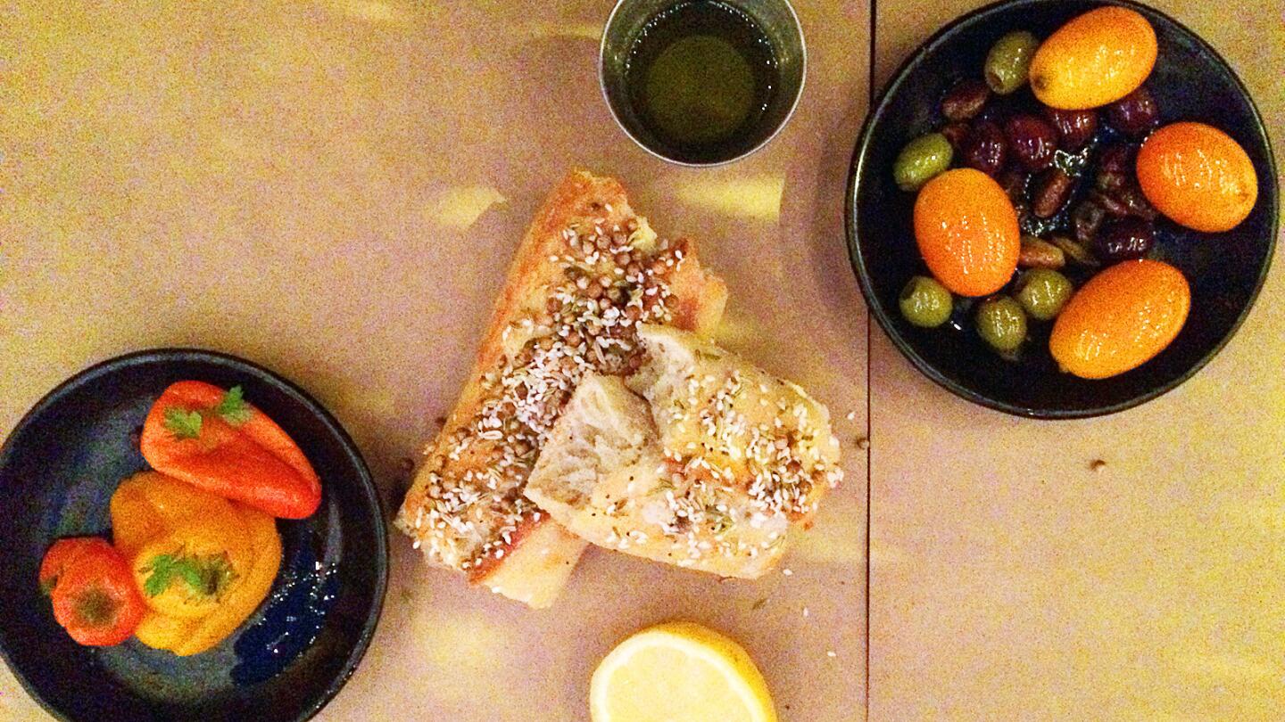 The table bread with olive oil, a lemon, marinated kumquats, olives and pistachios and pickled peppers.