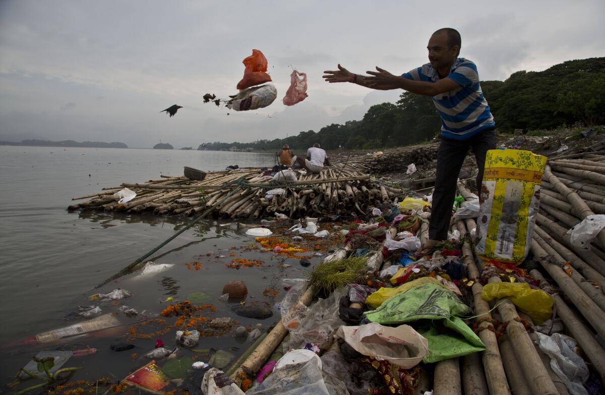 A Hindu devotee throws flowers and plastic bags into a river.