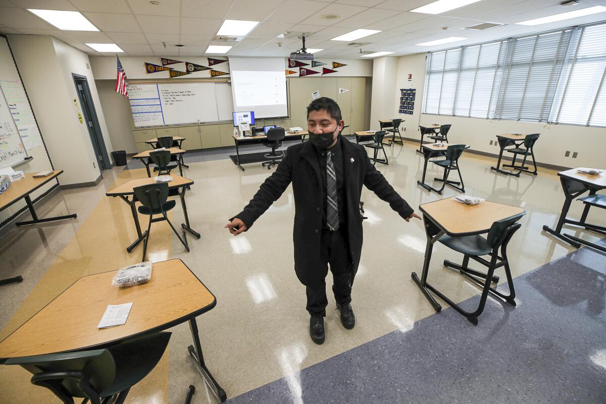 A man points to desks spaced apart in a high school classroom