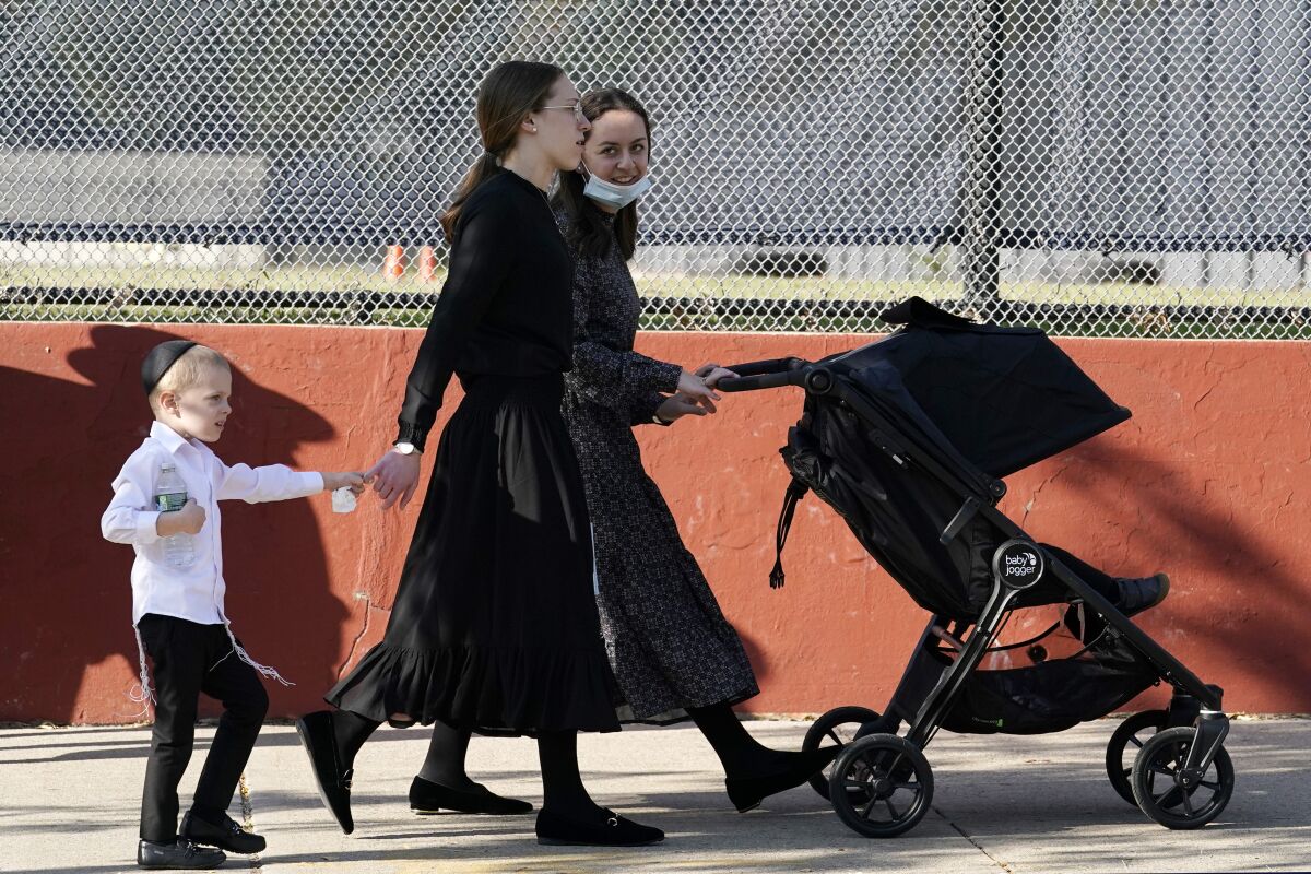 Two young women walk with children during the Jewish holiday of Sukkot, Sunday, Oct. 4, 2020, in the Borough Park neighborhood of New York. New York City's mayor says he has asked the state for permission to close schools and reinstate restrictions on nonessential businesses in several neighborhoods because of a resurgence of the coronavirus. Shutdowns would happen starting Wednesday in nine zip codes in the city, including Borough Park. (AP Photo/Kathy Willens)