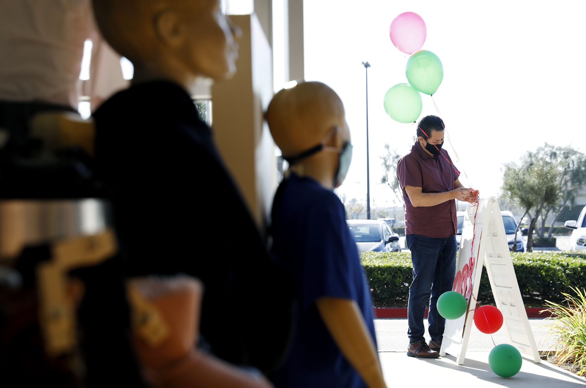 Carlos Salas puts balloons on a sign on the sidewalk of his business 4Kids Clothes in Anaheim.
