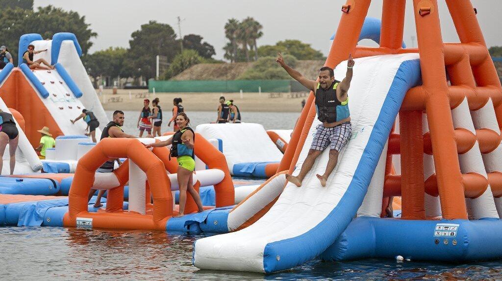 Daily Pilot sports editor Steve Virgen, right, slides through the finish line during the second annual Liquid Run, a floating obstacle course, at Newport Dunes Waterfront Resort on Saturday morning in Newport Beach.