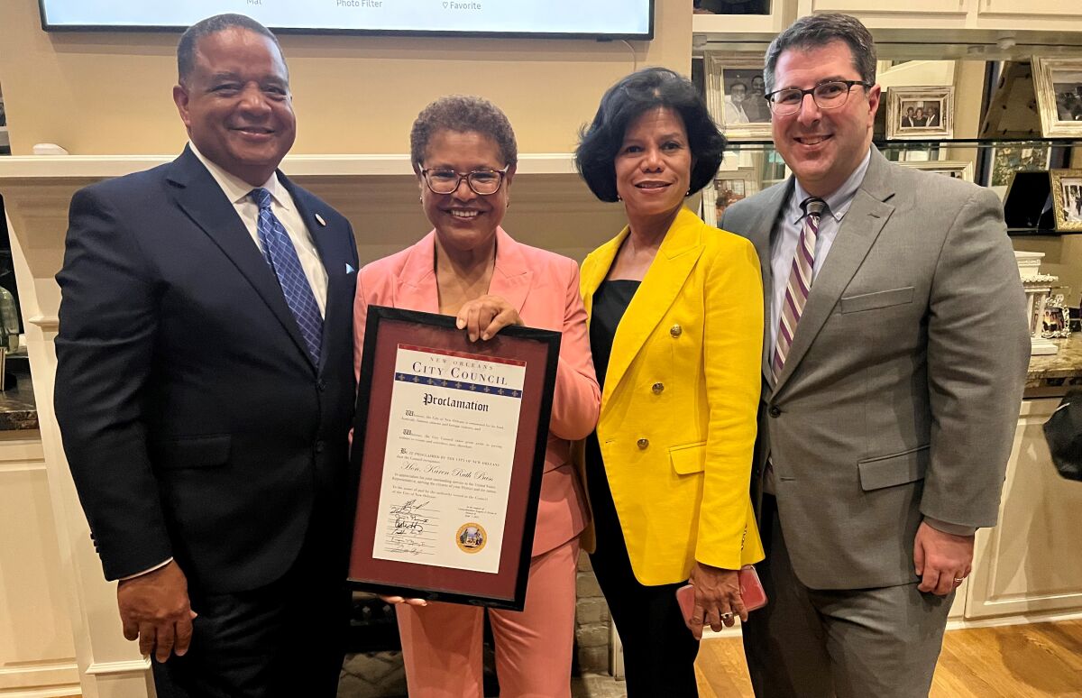 Two men and two women pose together for a photo, smiling. The men are in suits, the women in pant suits.