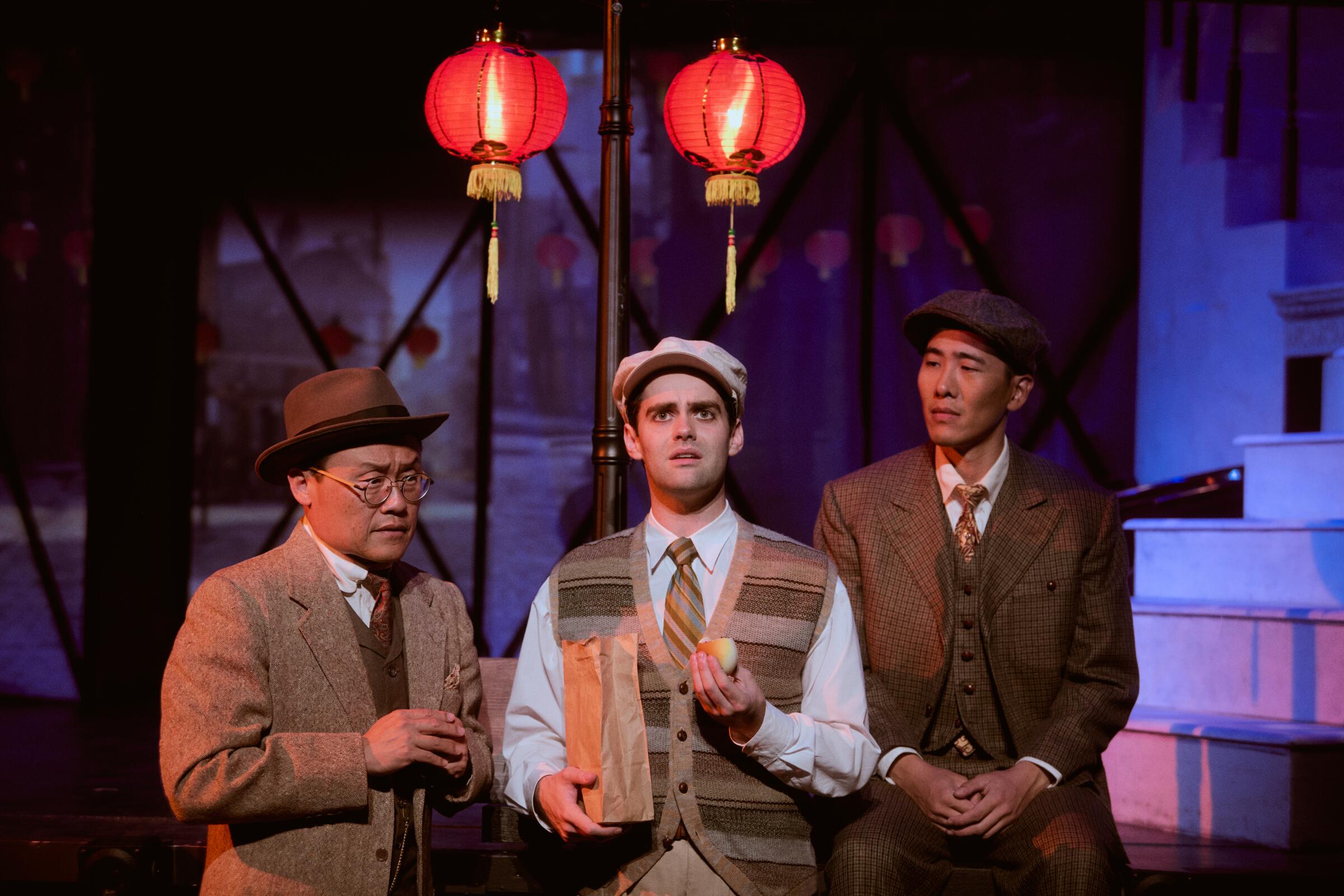 Three men stand onstage in front of Chinese lanterns