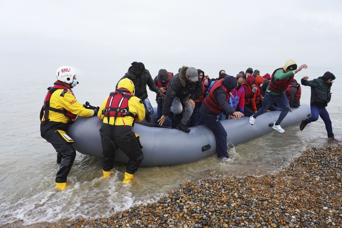 FILE - A group of people thought to be migrants are helped ashore by lifeboat crew members, after arriving on a dinghy at a beach in Dungeness, in south east England, Saturday, Nov. 20, 2021. A U.K. parliamentary committee on Wednesday Dec. 1, 2021, criticized government plans to deter migrants from trying to reach Britain in small boats, saying the measures will endanger lives without stopping dangerous journeys like the one that killed 27 people last week. (Gareth Fuller/PA via AP, File)