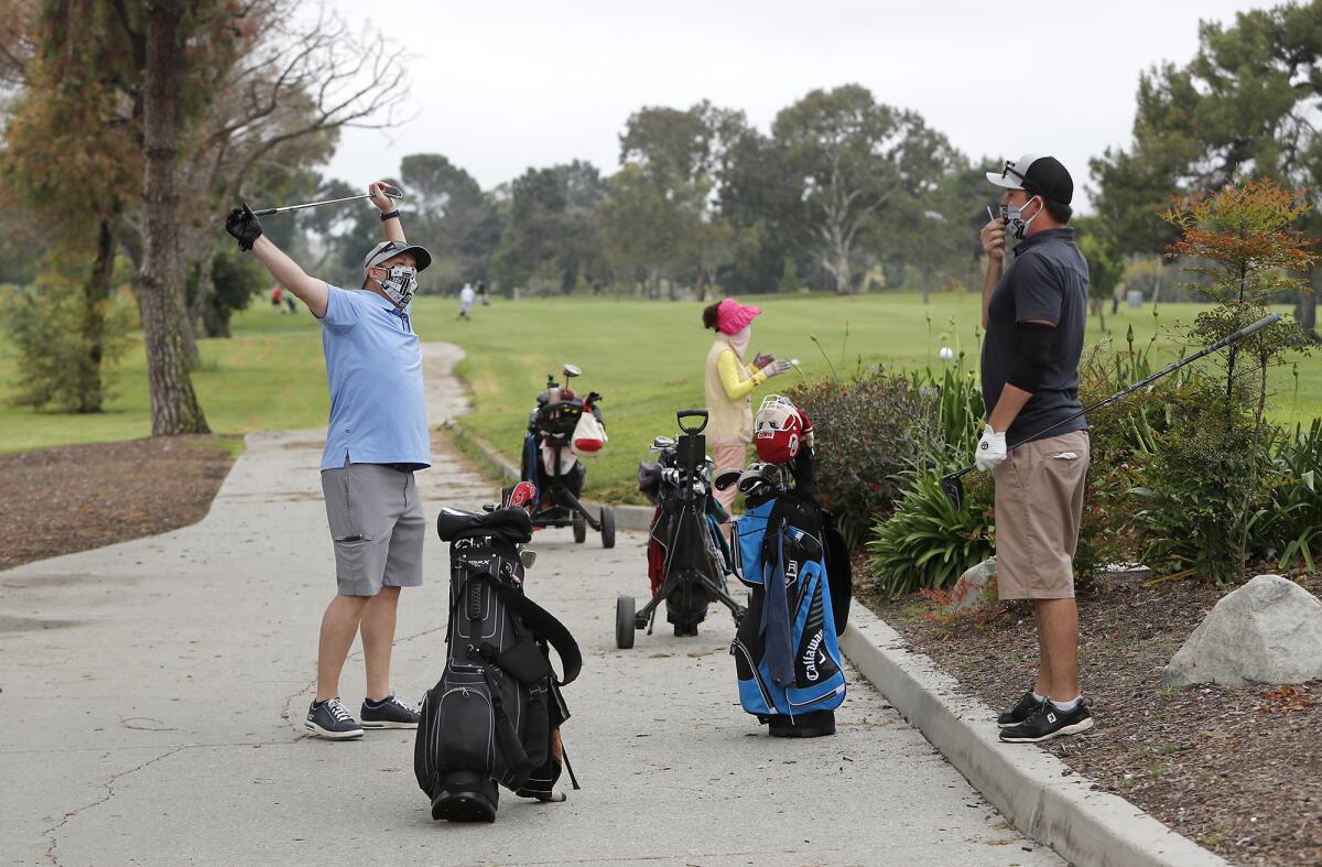 Golfers Tom Moody, left, 45, of Rancho Cucamonga and Gary Henson, right, 37, a club member, practice social distancing as they wait to tee off at Costa Mesa Country Club on Wednesday.