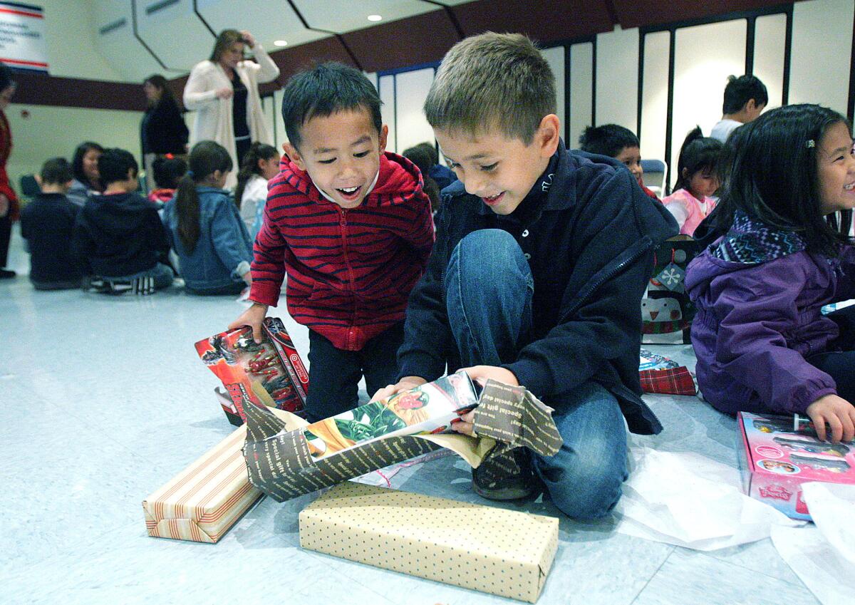 Geronimo Antonio, 6, looks at the gifts that Eric Tarebedian, 7, is unwrapping at Cerritos Elementary School on Monday, Dec. 14, 2015.