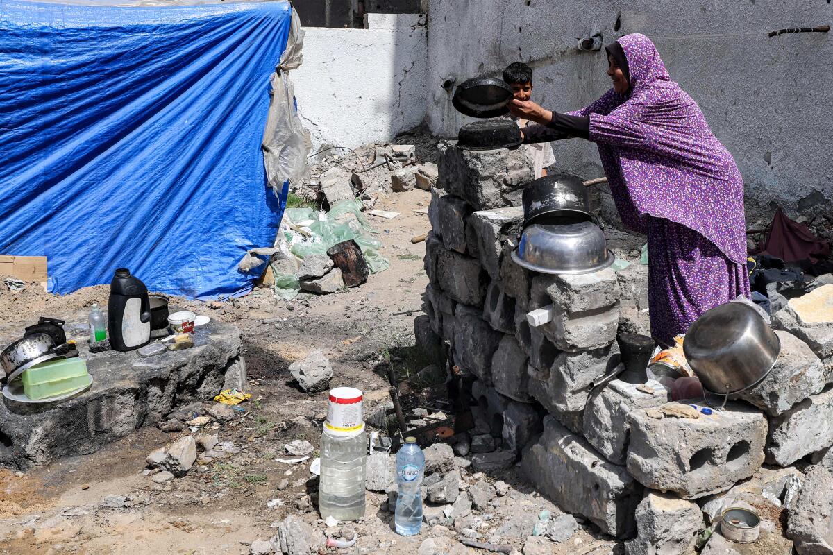 A woman washes pots outside a tent pitched amid rubble 