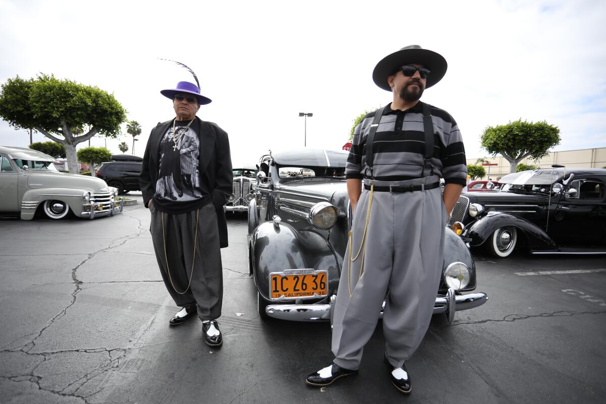Two men in zoot suits in a lot full of cars.