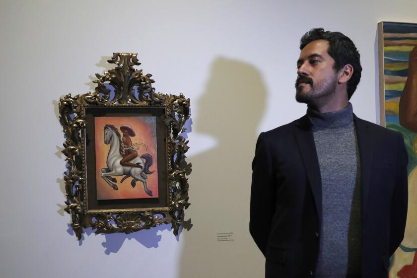 Mexican artist Fabian Chairez stands next to his painting showing Mexican Revolution hero Emiliano Zapata straddling on a horse nude, wearing high heels and a pink, broad-brimmed, during an interview at the Fine Arts Palace in Mexico City, Wednesday, Dec. 11, 2019. Mexico President Andres Manuel Lopez Obrador says he'll ask his culture minister to mediate a dispute over an effeminate painting of Zapata. (AP Photo/Marco Ugarte)