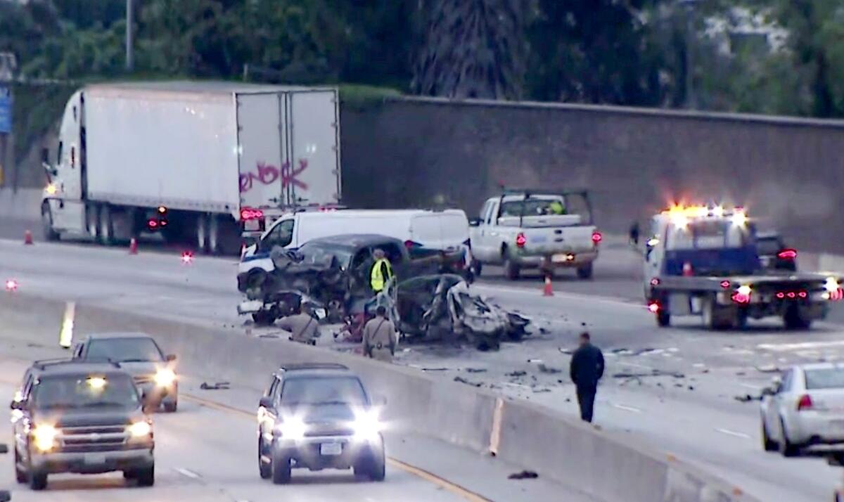 Burned wreckage of vehicles on a closed freeway with a tow truck and authorities nearby