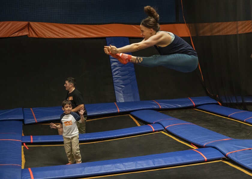 A child watches a woman bounces on a trampoline and touches her toes.