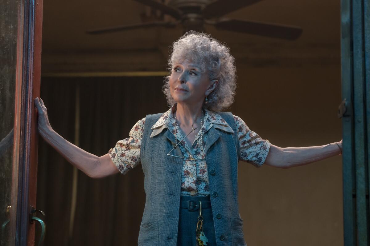 A woman in a floral top and blue vest stands in a doorway in "West Side Story."