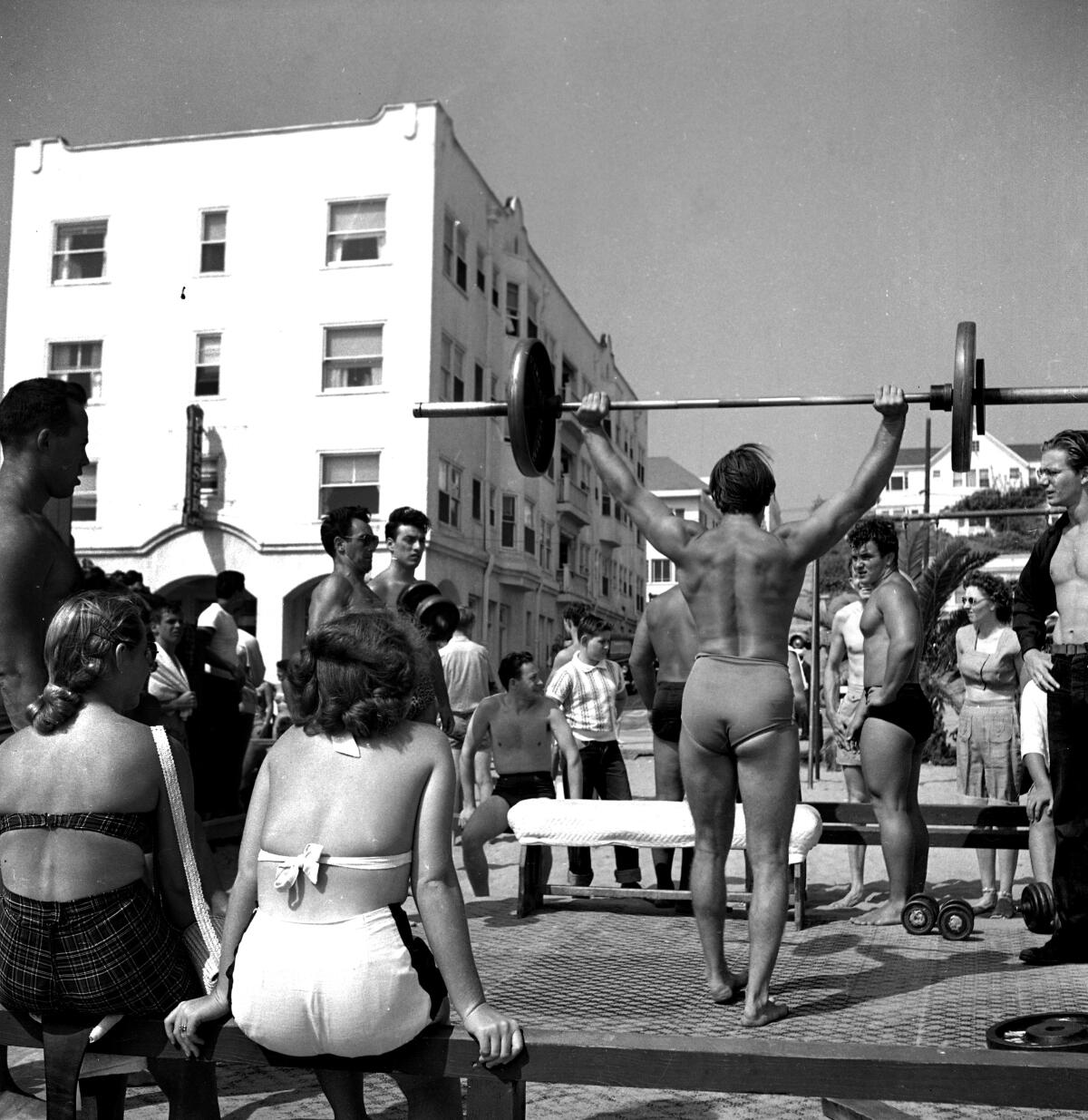 A muscled shirtlesss man lifts weights at Muscle Beach in Santa Monica,1949.