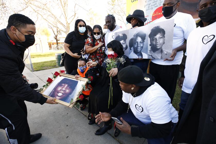 LOS ANGELES, CA - MARCH 16: Filmmaker Shannon Dion, left, places a portrait for a photo to the family of Latasha Harlins a 15-year-old Black girl who was fatally shot by a Korean liquor store owner in March 1991 over a dispute involving a bottle of orange juice as family, close friends and community members marked the 30th anniversary since Latasha's death and announced the naming of the playground at the Algin Sutton Recreation Center at 8800 S. Hoover St. in her honor. Latasha and her friends played in the park growing up as children. Algin Sutton Recreation Center on Tuesday, March 16, 2021 in Los Angeles, CA. (Al Seib / Los Angeles Times).