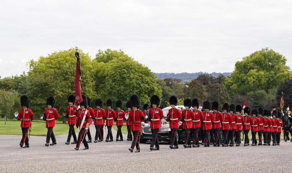 Soldiers in red jackets escort a hearse carrying the coffin of Queen Elizabeth II in the royal funeral procession