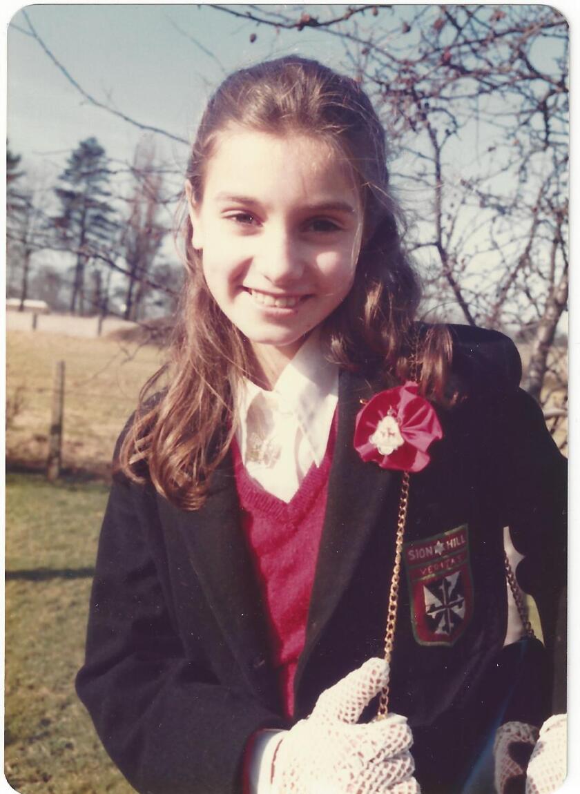 A photograph of Sinéad O'Connor in primary school days, wearing a school uniform and white knit gloves.