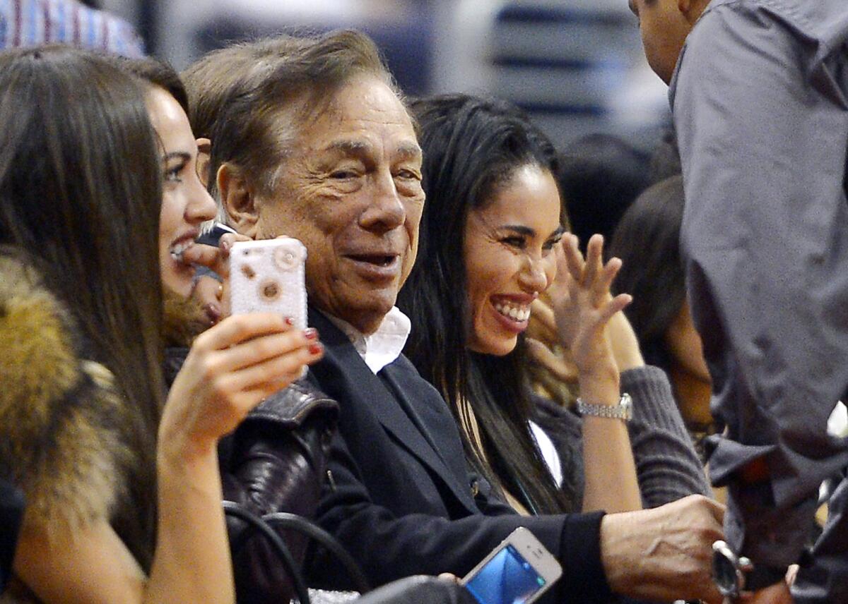 Clippers owner Donald Sterling, center, sits with V. Stiviano, right, at Staples Center during a game against the Sacramento Kings on Oct. 25, 2013. The NBA is investigating a report of an audio recording in which a man purported to be Sterling makes racist remarks while speaking to Stiviano.