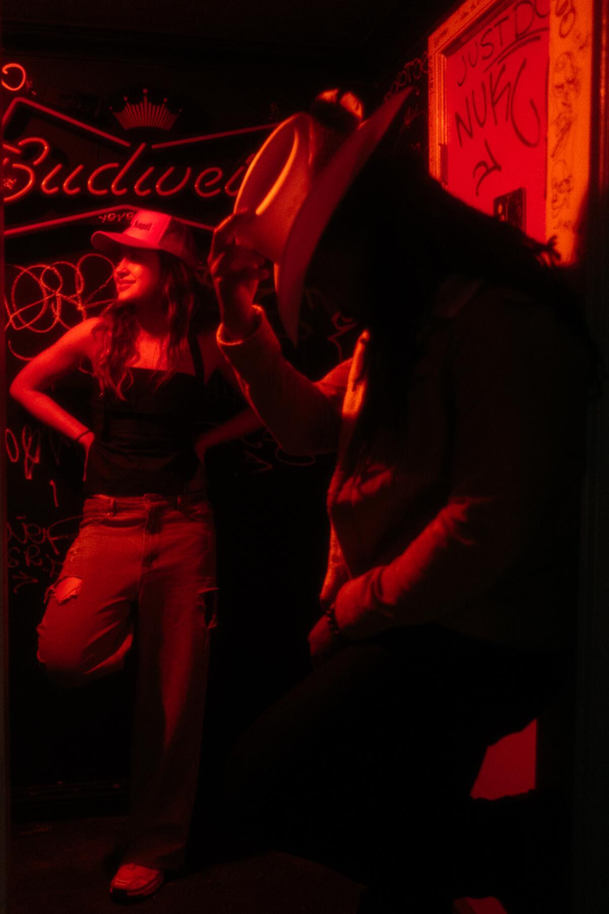 A man and a woman in cowboy hats stand under dramatic red lighting