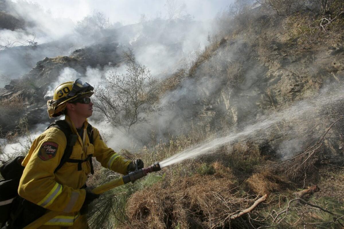 A firefighter sprays water on smoldering brush on a hillside along California 39 in Azusa.