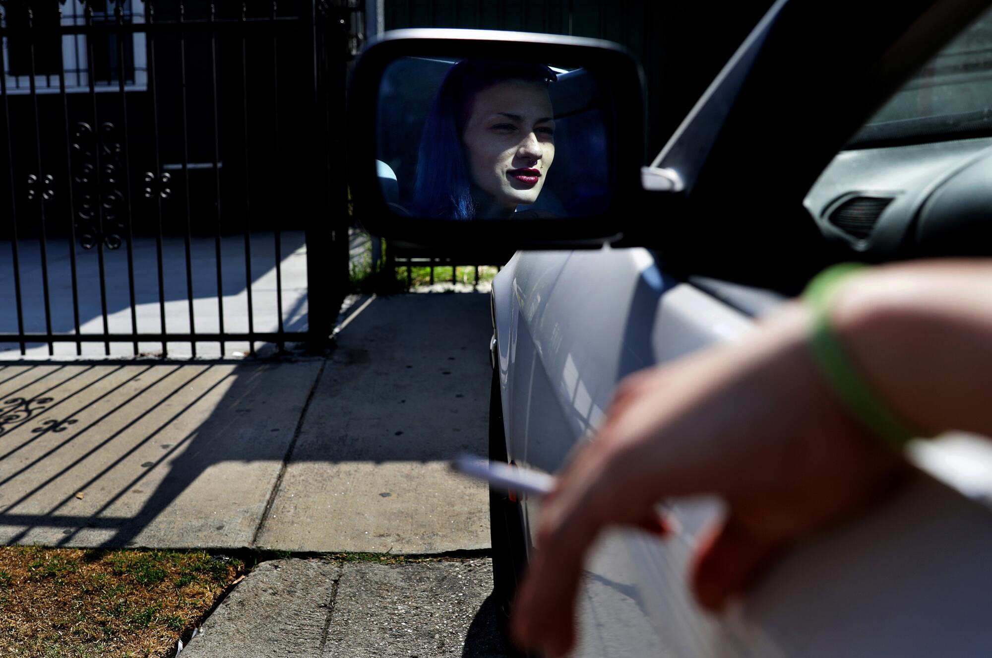 A woman sitting inside a car as seen in the driver side mirror.