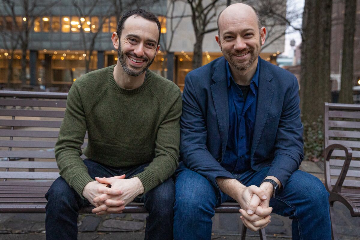 Brothers Brandon and Lance Kramer sit on a bench outdoors and smile for the camera.
