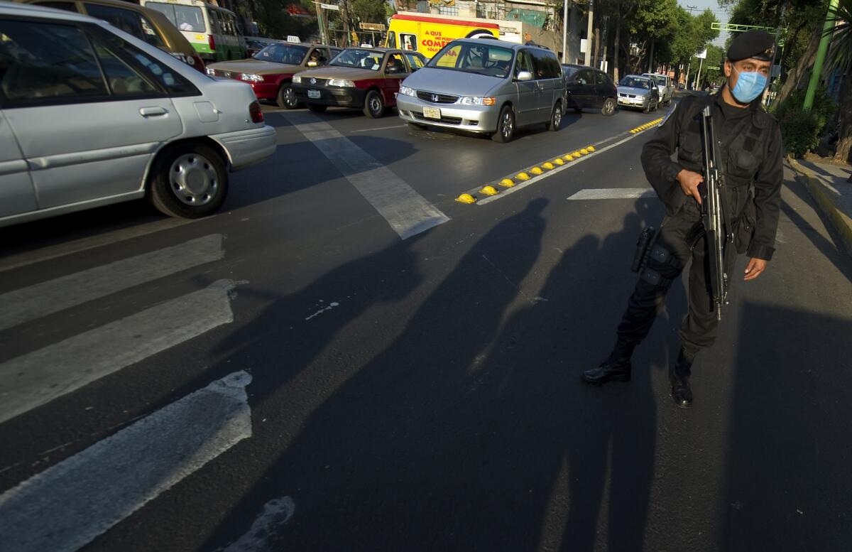 A police officer with a rifle stands guard on a street beside vehicles