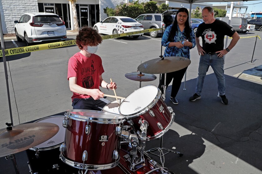 Joseph Mintz, left, plays a drum set as Marielena Teng, Mira Mesa High School choir teacher, and Tom Stewart look on. 
