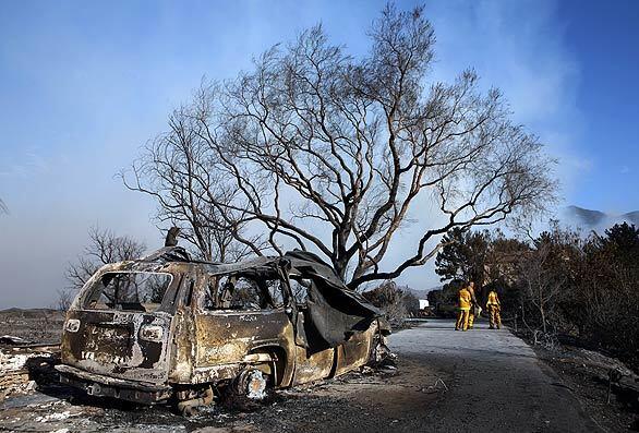 Los Angeles city firefighters return to the spot on Holly Road where a battalion chief's truck burned Wednesday as flames swept through the Mission Canyon area of Santa Barbara, destroying nearly two dozen homes.