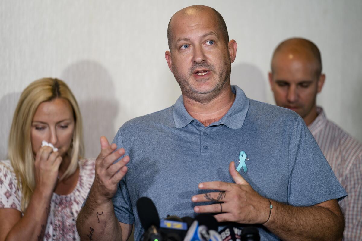 A man speaks at a microphone with a woman and another man behind him