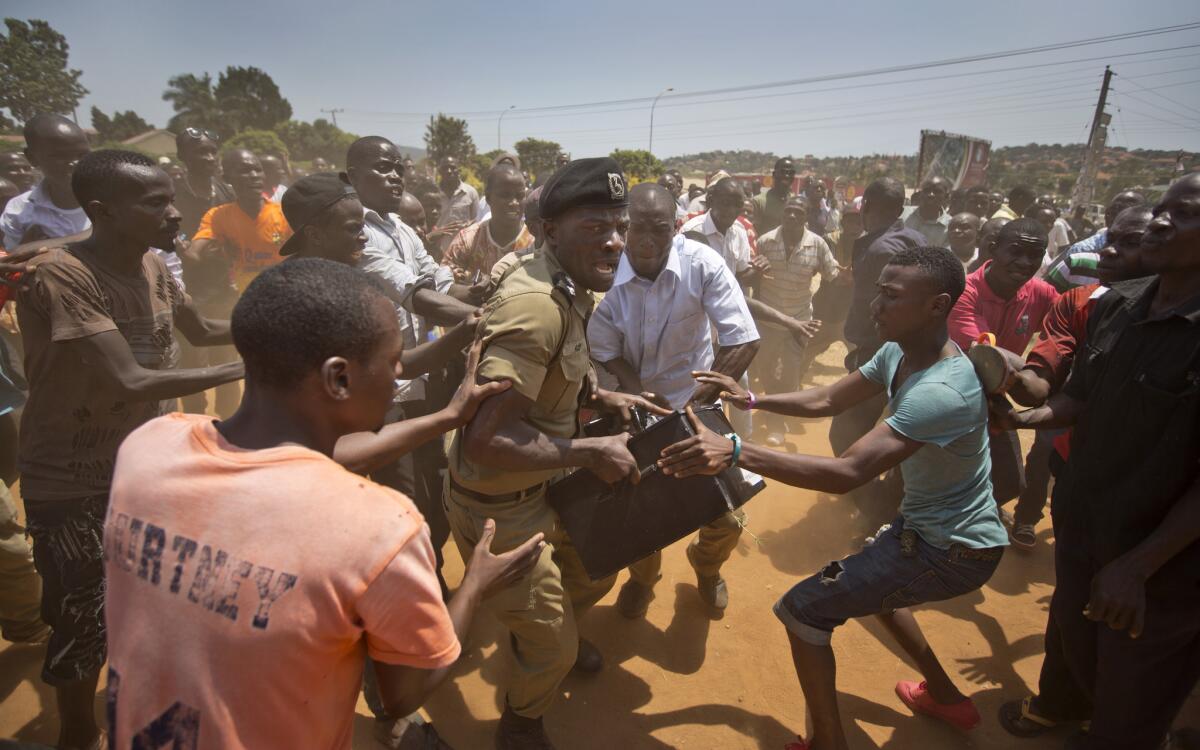 A Ugandan policeman struggles to keep his hold on a box containing voting materials, as excited voters surround him after waiting for hours to cast ballots in Ggaba.