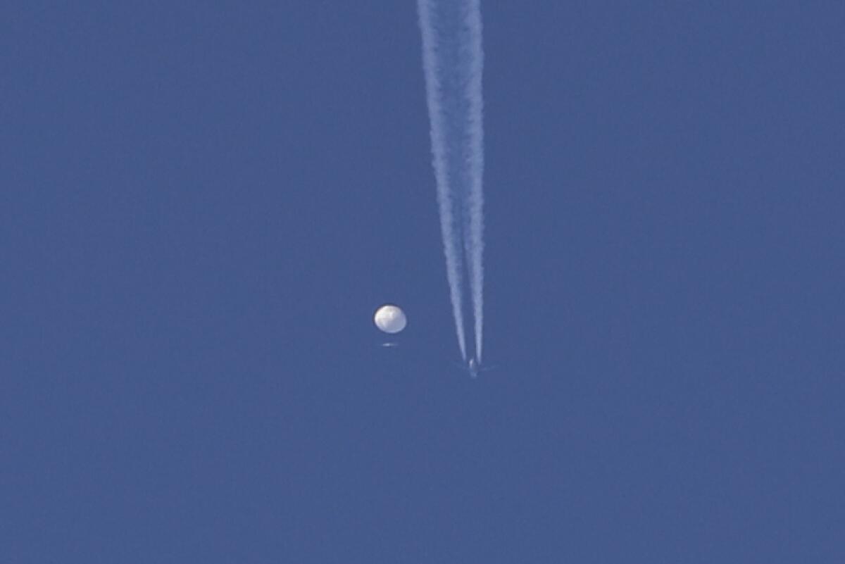 A large balloon drifts above the Kingston, N.C., area, with an airplane and its contrail near it.