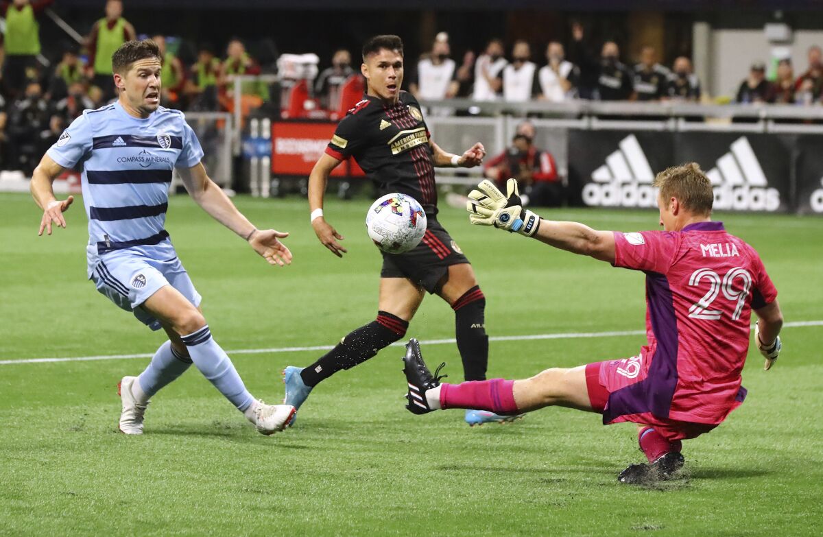 Atlanta United attacker Luiz De Araujo, center, scores a goal past Sporting Kansas City goalkeeper Tim Melia, right, but was injured on the play and had to come out of an MLS soccer match Sunday, Feb. 27, 2022, in Atlanta. (Curtis Compton/Atlanta Journal-Constitution via AP)