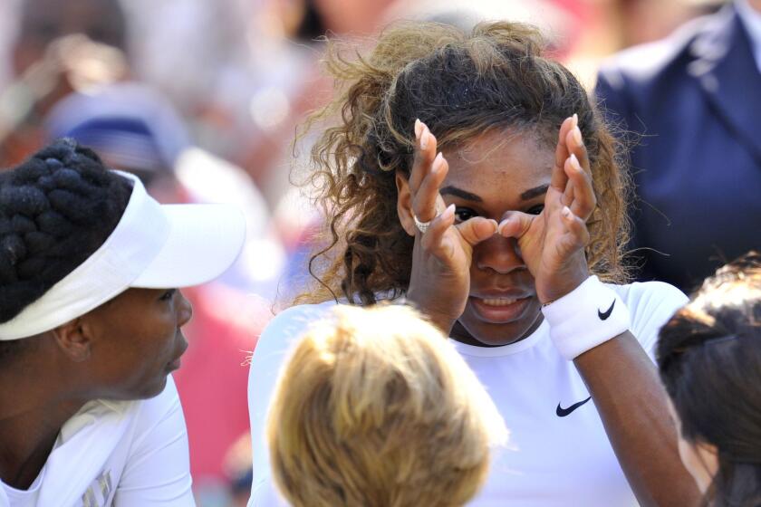 Serena Williams, sitting next to sister Venus, wipes her face as she talks to a doctor Tuesday at Wimbledon.