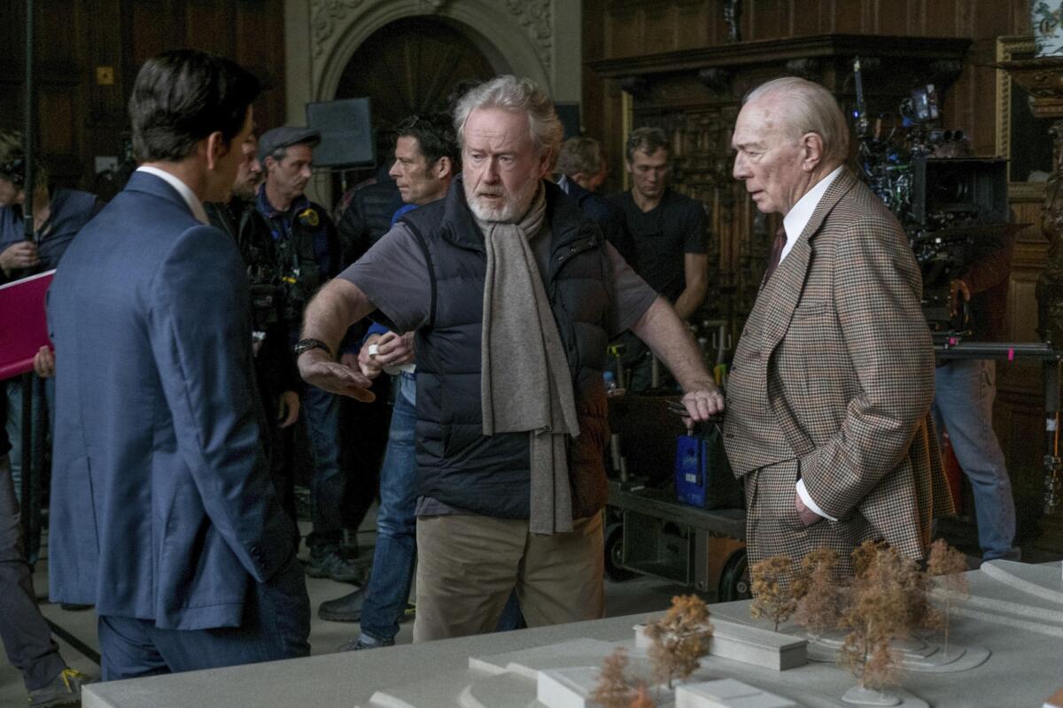 Ridley Scott directs actors Mark Walhlberg and Christopher Plummer, who are dressed in fine suits
