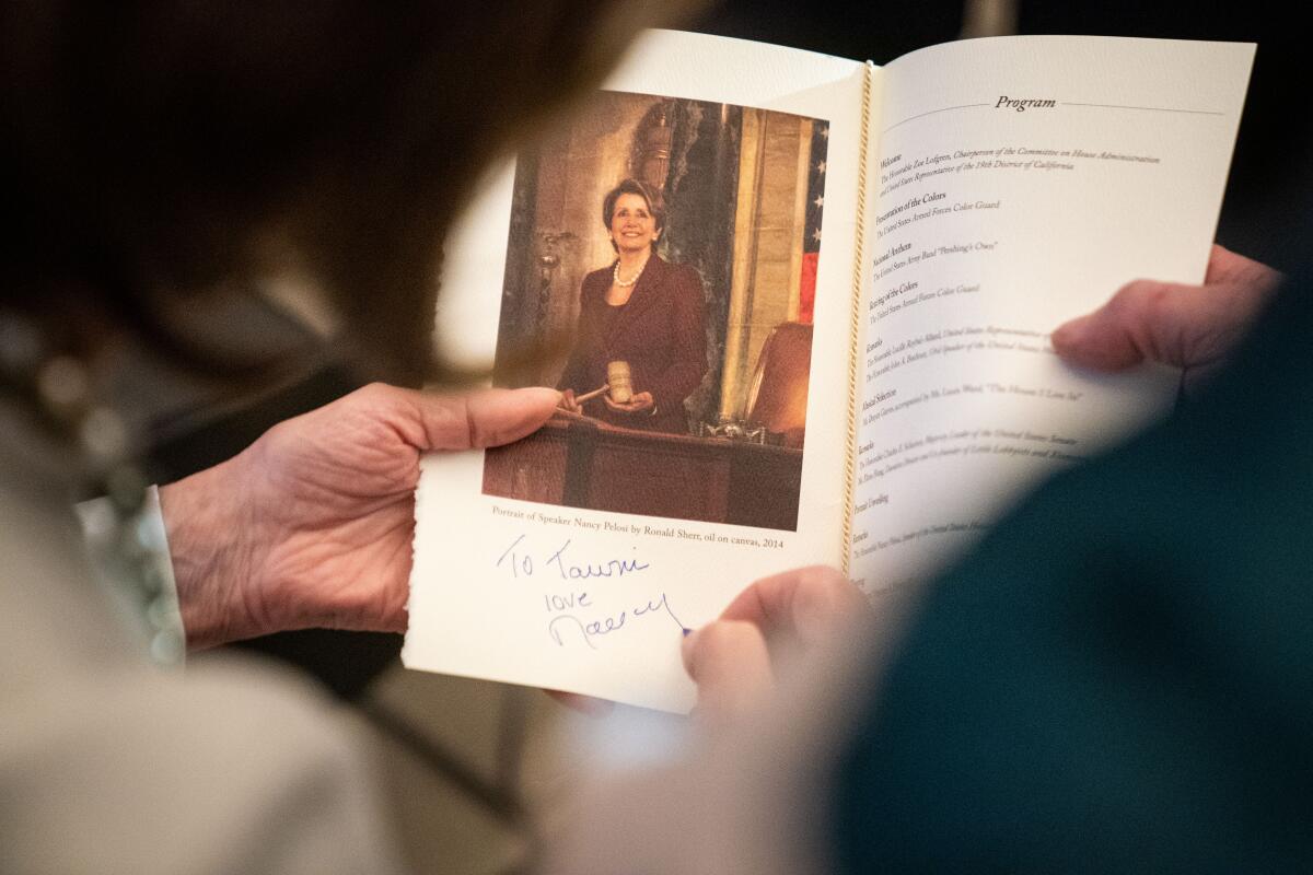Nancy Pelosi signs a program underneath an image of her portrait.