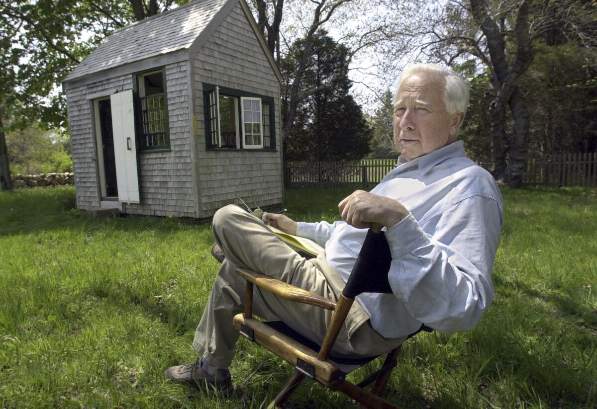 A gray-haired man sits in a chair outside, near a small shed.