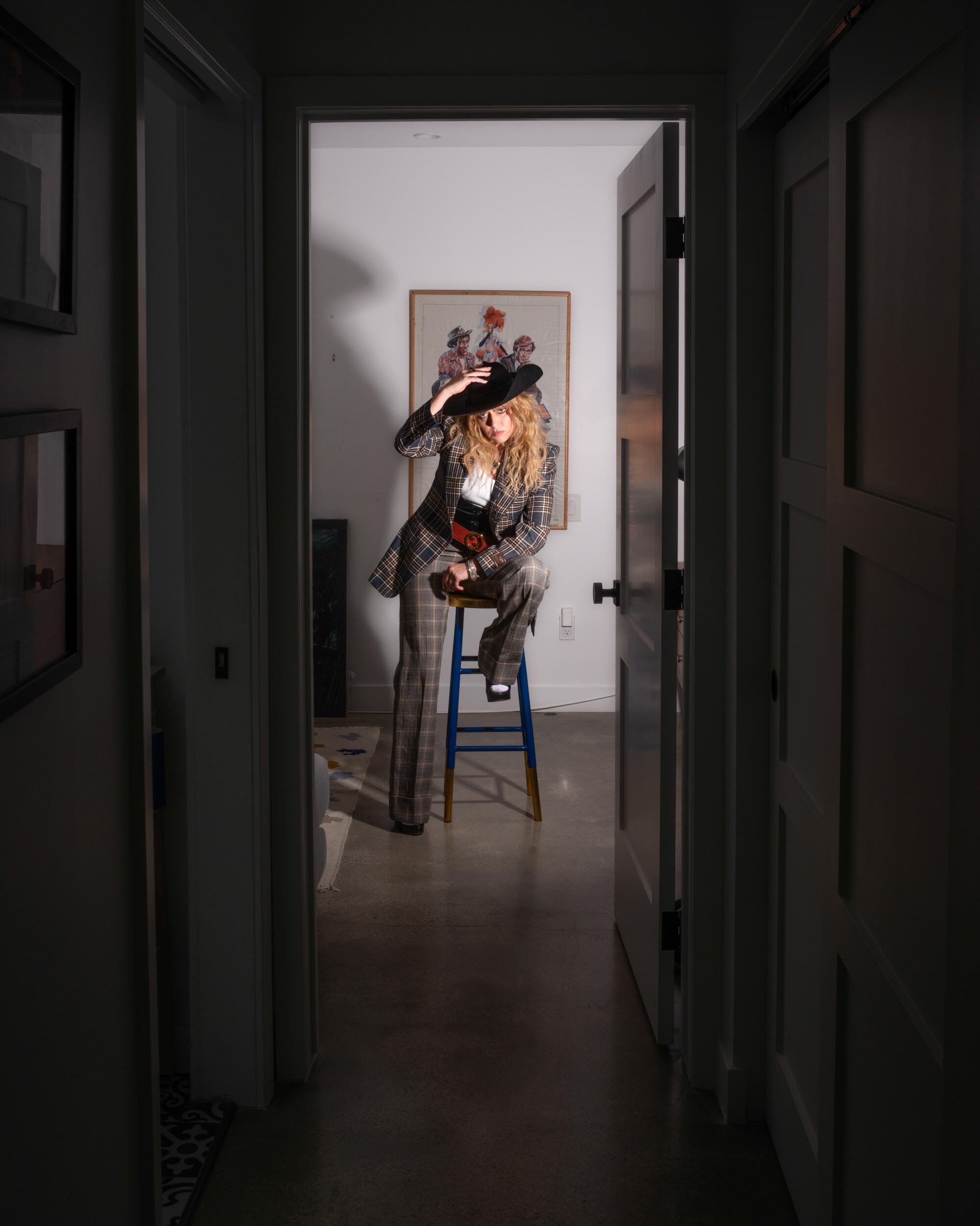 A woman sits on a stool at the end of a dark hallway
