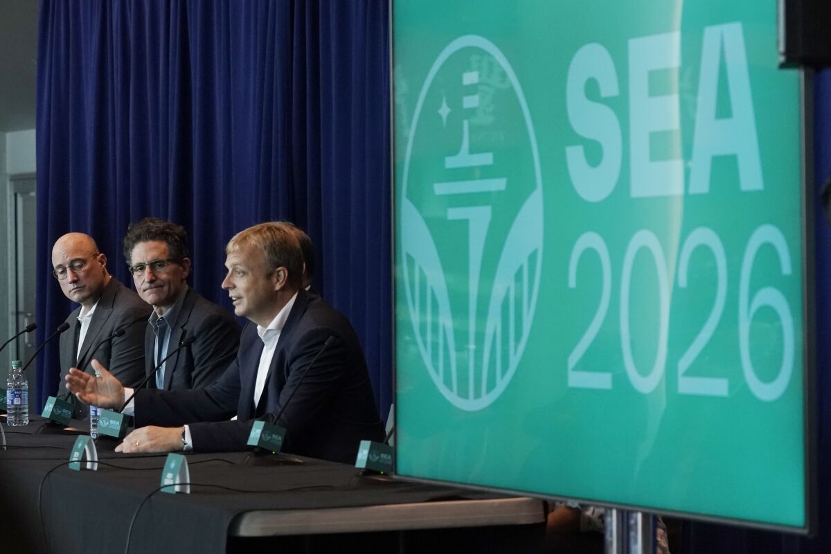 Colin Smith, right, FIFA chief tournaments and events chairman, speaks Monday, Nov. 1, 2021, in Seattle as Adrian Hanauer, center, owner of the MLS soccer Seattle Sounders, and Kasey Keller, left, former goalkeeper for the Sounders and the U.S. Men's National Team, look on during a news conference at Lumen Field. Smith was discussing taking part in an official visit of a FIFA delegation to Seattle, as organizers try to be selected as a host city for the FIFA World Cup in 2026. (AP Photo/Ted S. Warren)
