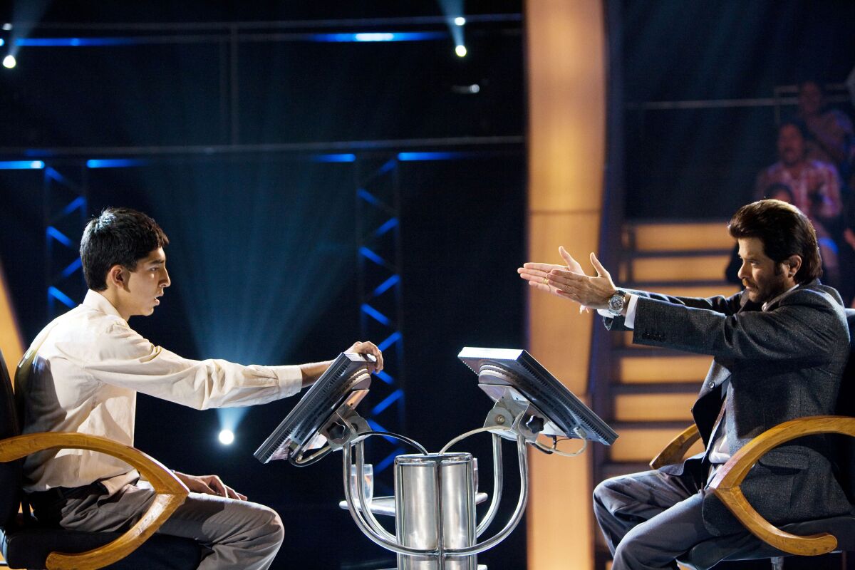 Dev Patel looks at a computer as Anil Kapoor gestures to him with his arms in a scene from "Slumdog Millionaire"