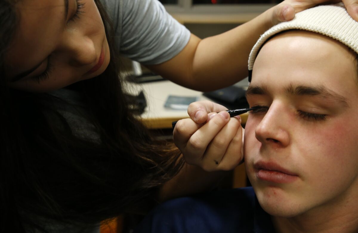 MacKale McGuire closes his eyes while Haley Butkovich, a fellow senior and cast member, applies eye makeup before their school's dress rehearsal of Disney's "High School Musical" on Wednesday, Feb. 9, 2022 in Cadillac, Mich. McGuire, a cancer survivor whose left leg was amputated above the knee in 2018, was one of the lead actors in the musical. (AP Photo/Martha Irvine)