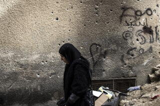 A Palestinian woman walks past a wall riddled with bullet holes