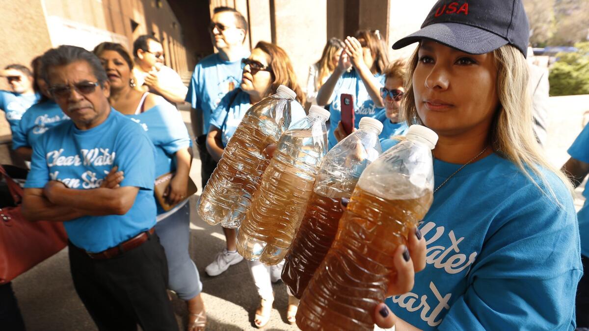Compton resident Lucia Camacho holds bottles of brown water that she says were collected from taps in Compton.