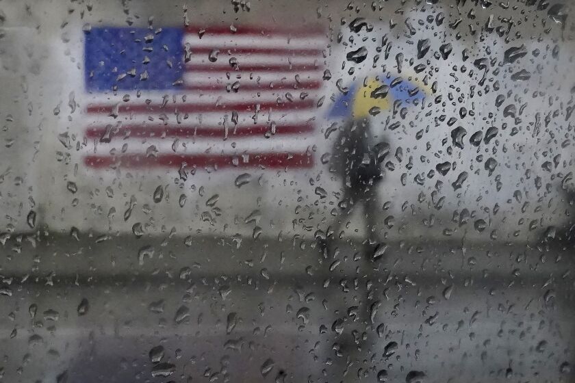 FILE - A pedestrian carries an umbrella while walking past a painting of an American flag in San Francisco, Jan. 11, 2023. A new study says the drenching that California has been getting since Christmas will only get wetter and nastier with climate change. (AP Photo/Jeff Chiu, File)