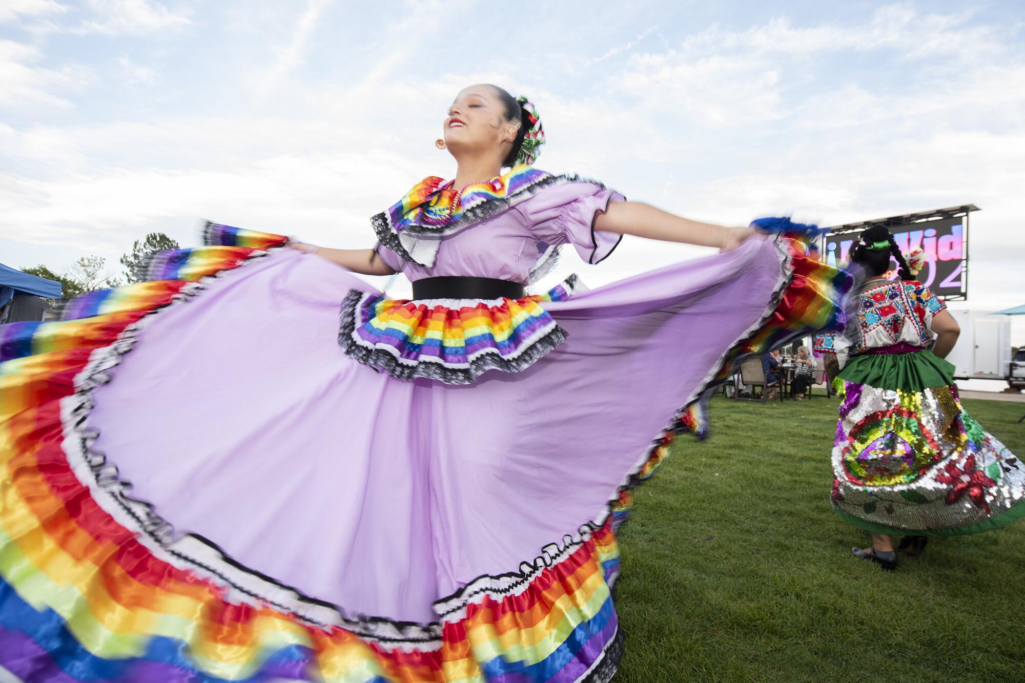 A woman in a pale purple traditional dress with rainbow-colored trims spreads her skirt during a performance