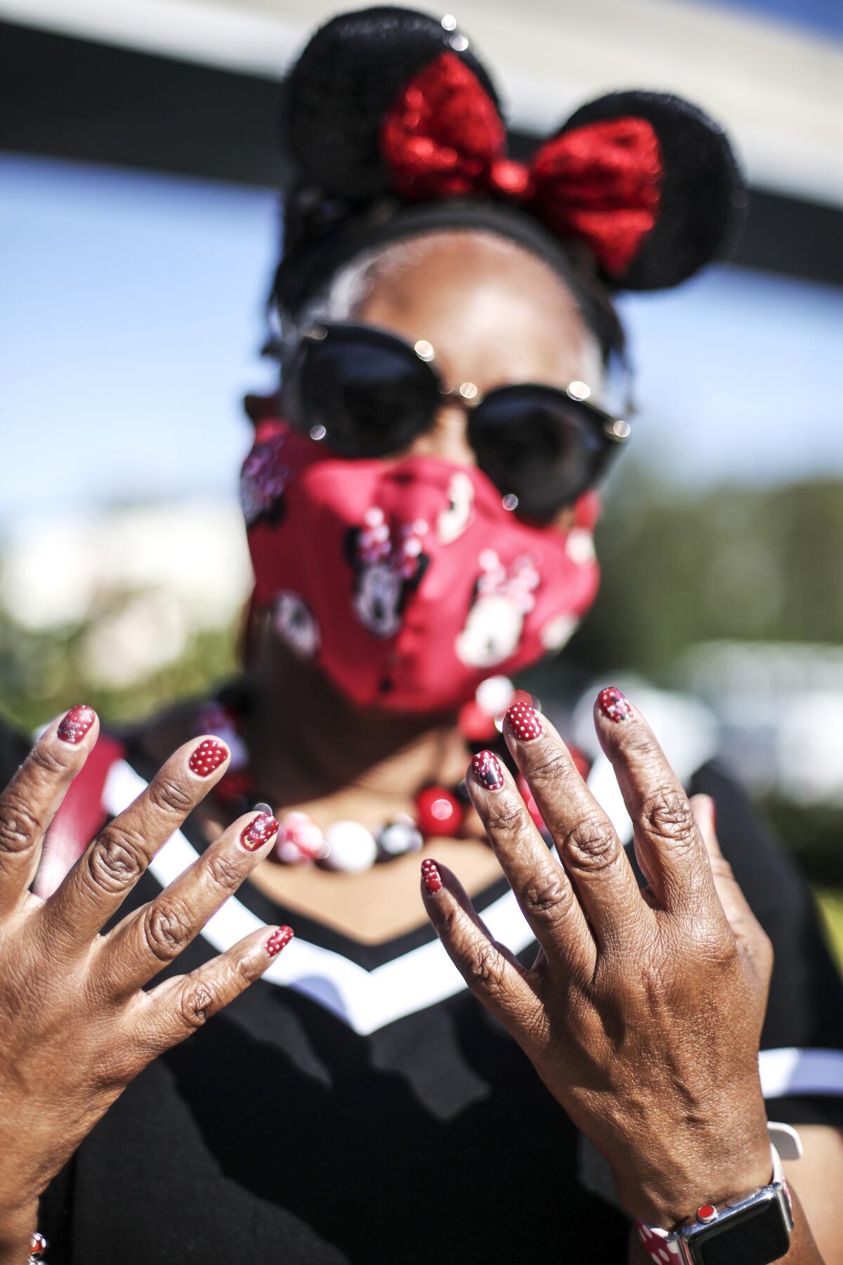 A woman in mask and mouse ears shows her white-dotted red fingernails