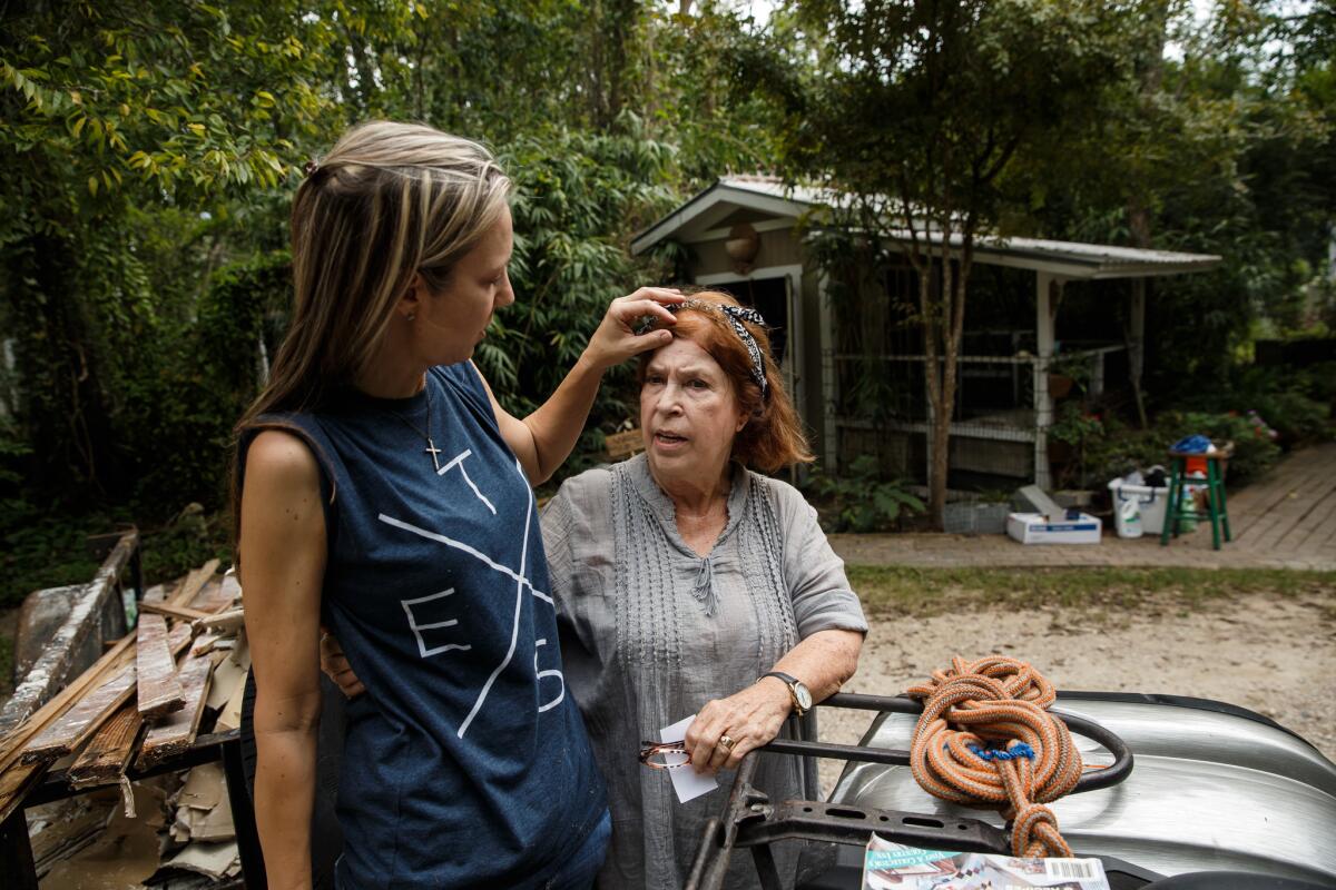 Jenny Sanders fixes Sue Bown's hair as they watch Sue's car get towed away after it was damaged by floodwaters. (Marcus Yam / Los Angeles Times)