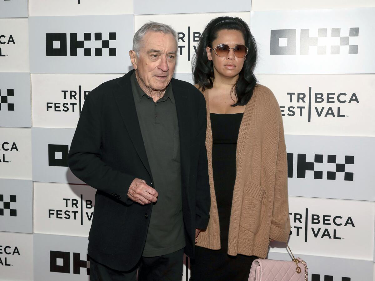 Actor Robert De Niro, left, and Tiffany Chen both wear jackets in front of a Tribeca Festival backdrop