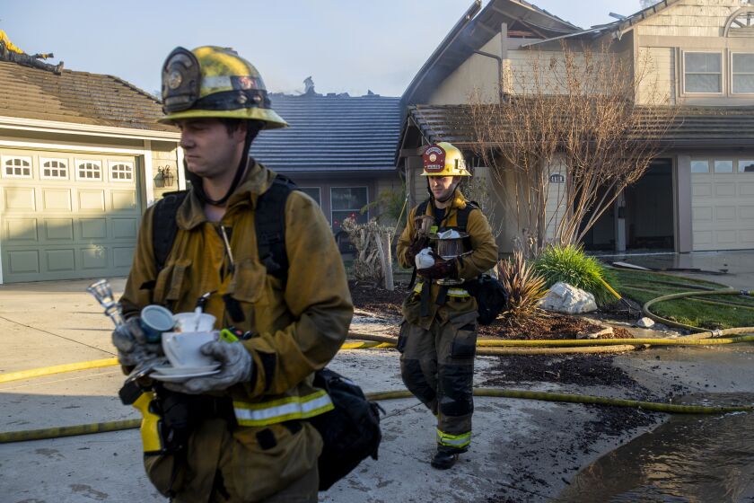 WHITTIER, CA - FEBRUARY 10, 2022: LA County firefighters carry valuables from a home destroyed by the Sycamore fire off Banyon Rim Drive on February 10, 2022 in Whittier, California. The wind driven Sycamore fire destroyed 2 homes and damaged a third. (Gina Ferazzi / Los Angeles Times)